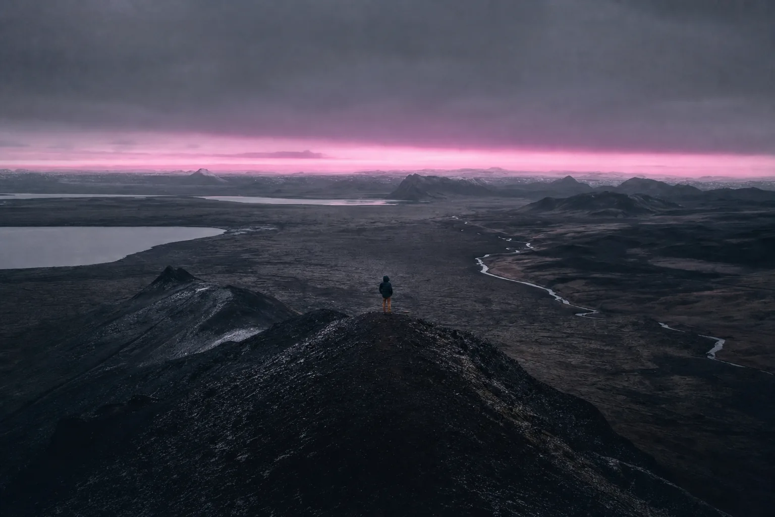 Paysage volcanique islandais au crépuscule : une bande magenta souligne l'horizon, une silhouette isolée se tient sur une crête.